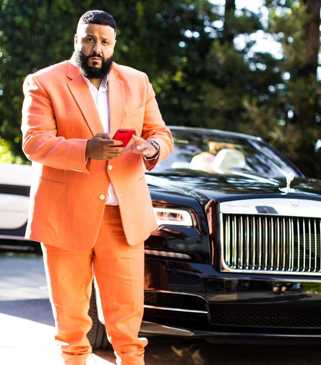 Man in a peach suit beside a black convertible